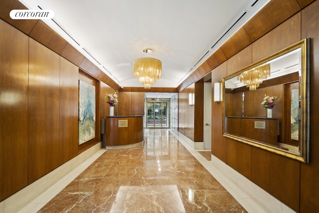 hallway featuring a notable chandelier, marble finish floor, and wooden walls