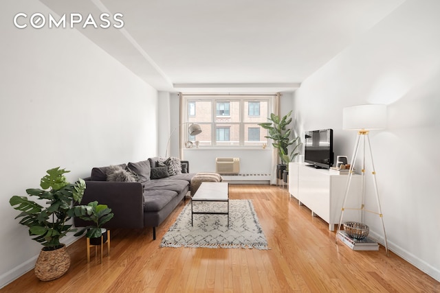 living area featuring light wood-style floors, baseboards, and an AC wall unit