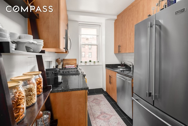 kitchen with dark tile patterned floors, backsplash, brown cabinets, a sink, and stainless steel appliances