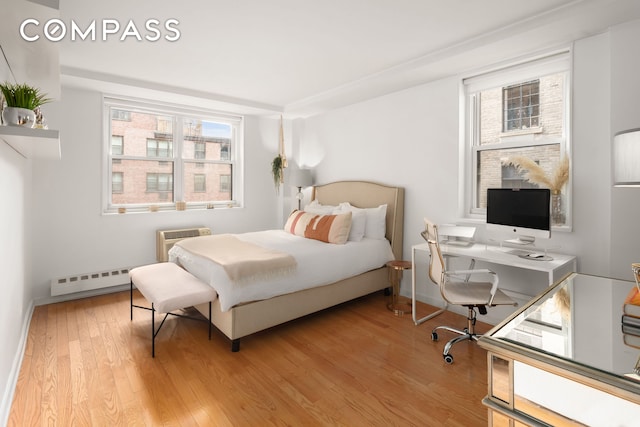 bedroom with light wood-style floors, baseboards, a baseboard heating unit, and a wall mounted air conditioner
