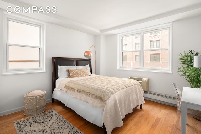 bedroom with baseboards, a wall mounted AC, a baseboard heating unit, and wood finished floors