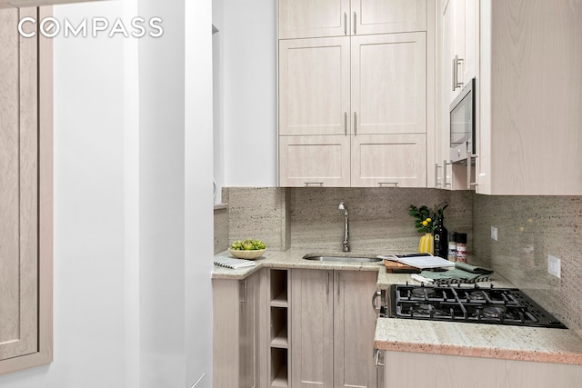 kitchen featuring light stone counters, a sink, cooktop, decorative backsplash, and stainless steel microwave