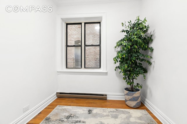 empty room with wood finished floors, baseboards, and a baseboard radiator