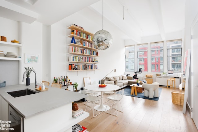 interior space with light wood finished floors, open shelves, beamed ceiling, light countertops, and a sink