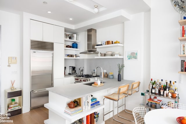 kitchen featuring open shelves, wall chimney range hood, built in fridge, and a sink