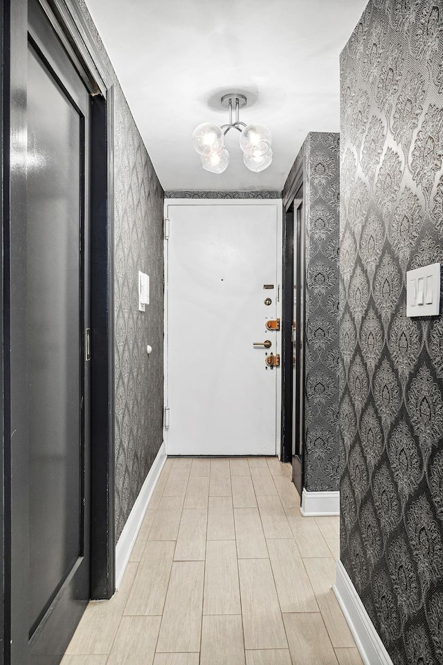 hall featuring wallpapered walls, an inviting chandelier, and baseboards