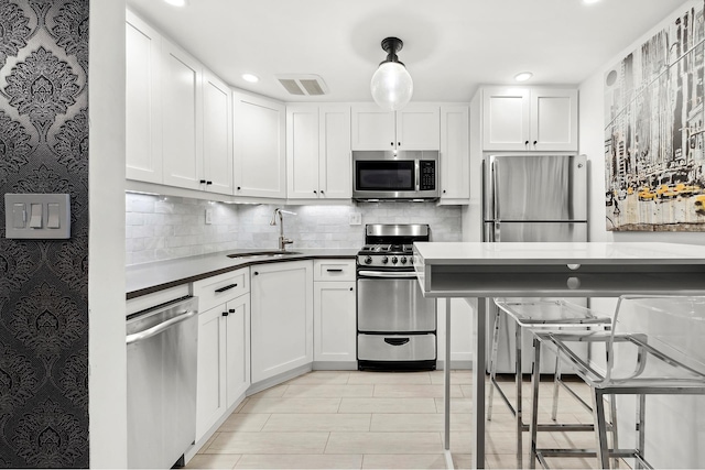 kitchen with visible vents, a sink, appliances with stainless steel finishes, dark countertops, and backsplash