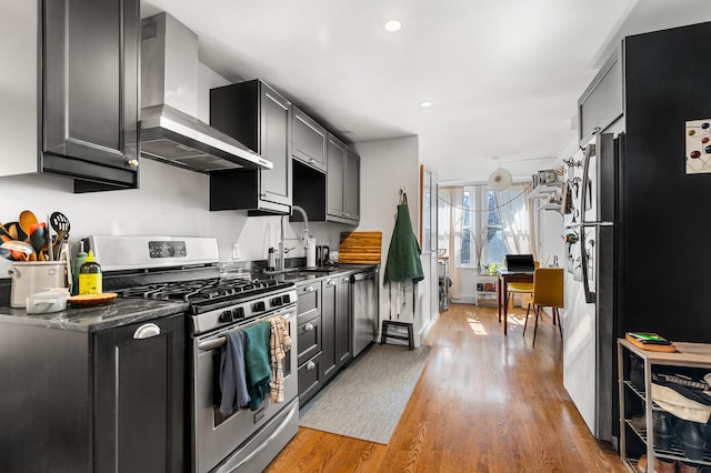kitchen featuring light wood-style flooring, recessed lighting, a sink, stainless steel appliances, and wall chimney range hood
