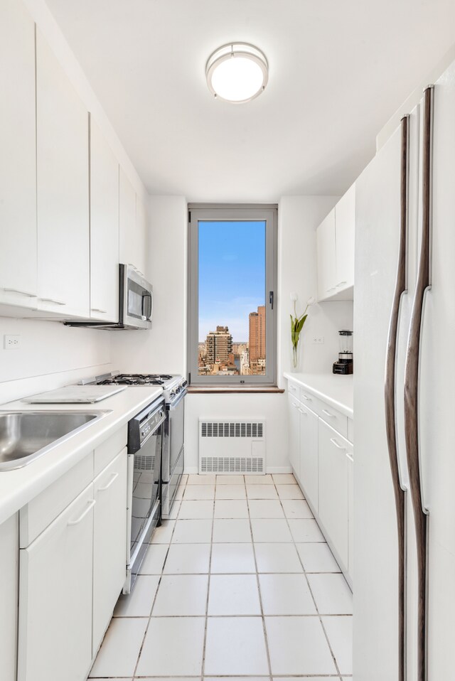 200 E 89th St Unit 30B, New York City, NY 10128 - kitchen with freestanding refrigerator, radiator heating unit, light countertops, white cabinetry, and stainless steel microwave