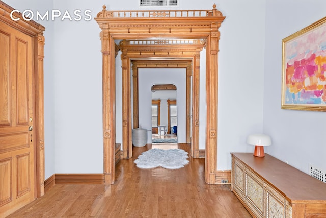 corridor with visible vents, baseboards, light wood-type flooring, french doors, and arched walkways