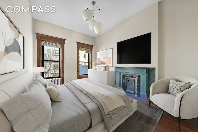 bedroom with radiator, wood finished floors, and a fireplace with flush hearth