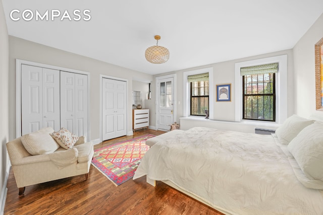 bedroom with two closets, baseboards, and dark wood-style flooring