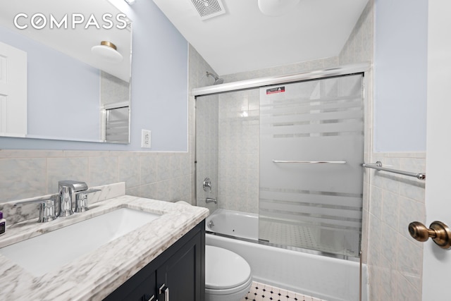 bathroom featuring visible vents, a wainscoted wall, toilet, combined bath / shower with glass door, and tile walls