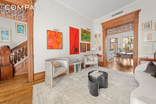 living room featuring wood finished floors, baseboards, visible vents, ornamental molding, and stairs