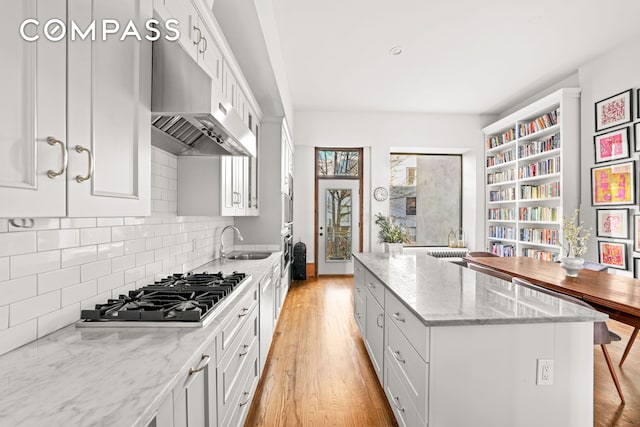 kitchen with light wood finished floors, a kitchen island, stainless steel gas cooktop, under cabinet range hood, and a sink