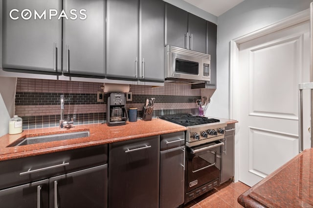 kitchen featuring appliances with stainless steel finishes, decorative backsplash, a sink, and light stone counters