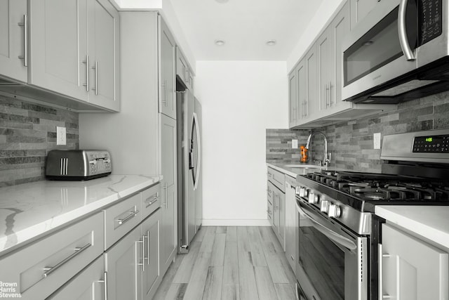 kitchen featuring stainless steel appliances, a sink, decorative backsplash, and light stone counters