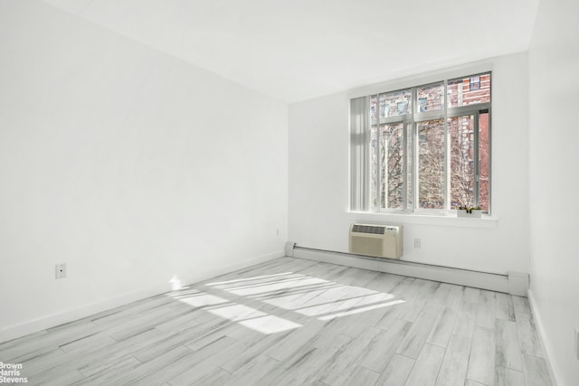 empty room with a baseboard heating unit, light wood finished floors, a wall mounted AC, and baseboards