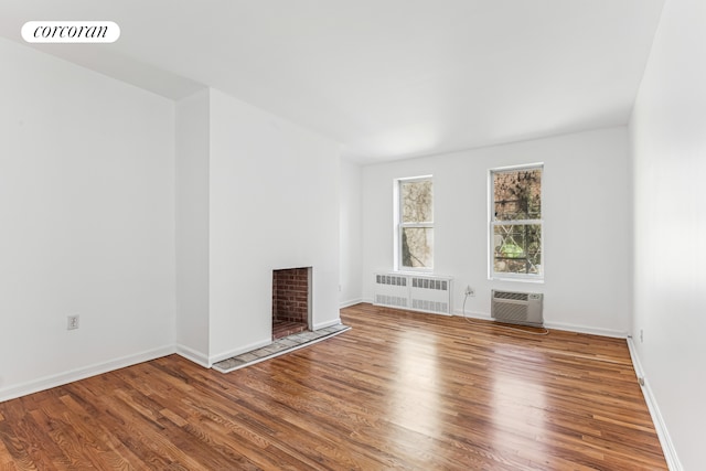 spare room with radiator heating unit, a fireplace with flush hearth, wood finished floors, and a wall mounted AC