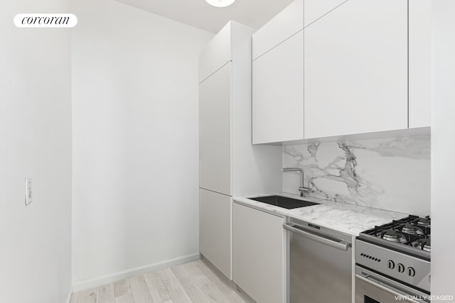 kitchen with appliances with stainless steel finishes, a sink, light countertops, white cabinets, and modern cabinets
