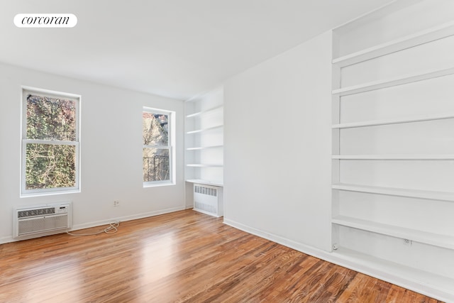 spare room with radiator heating unit, a wall mounted AC, built in shelves, wood finished floors, and baseboards