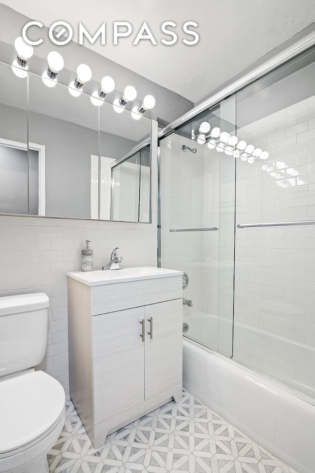 bathroom with vanity, toilet, tile walls, tile patterned floors, and enclosed tub / shower combo