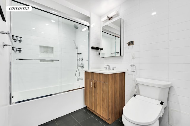 bathroom with bath / shower combo with glass door, toilet, tile walls, vanity, and tile patterned flooring