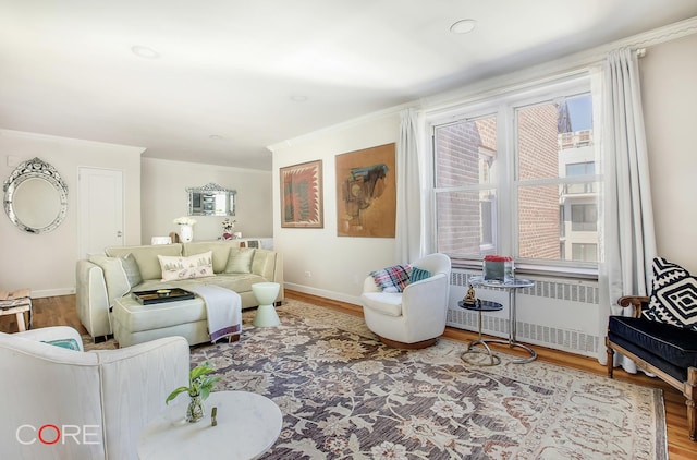 living room with radiator heating unit, wood finished floors, ornamental molding, and baseboards