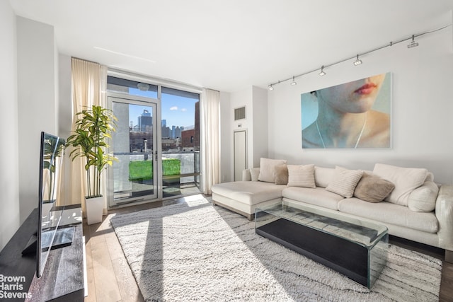 living area featuring rail lighting, floor to ceiling windows, a city view, and hardwood / wood-style flooring
