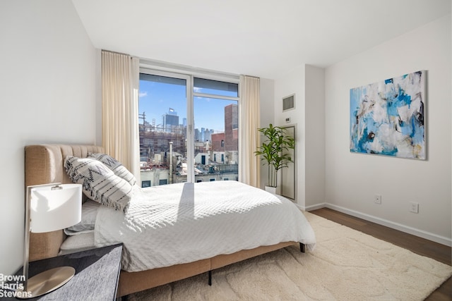 bedroom with a view of city, baseboards, visible vents, and wood finished floors