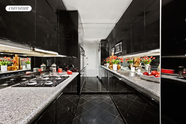 kitchen featuring dark cabinets, stainless steel microwave, black gas cooktop, light countertops, and a sink