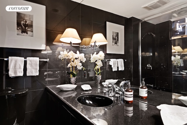 full bathroom with double vanity, visible vents, a sink, tile walls, and decorative backsplash