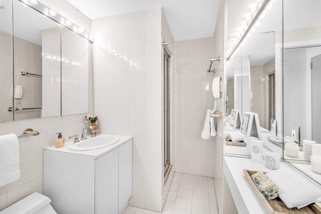 full bath with toilet, vanity, a stall shower, tile patterned floors, and tile walls