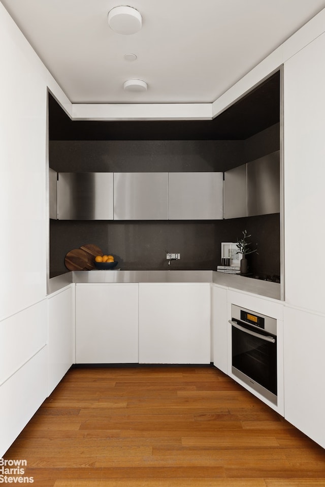15 William St Unit 33I, New York City, NY 10004 - kitchen featuring stainless steel oven, white cabinetry, light wood finished floors, and modern cabinets