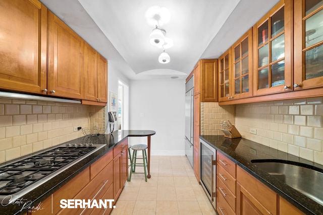 kitchen with wine cooler, appliances with stainless steel finishes, brown cabinets, light tile patterned floors, and dark stone counters
