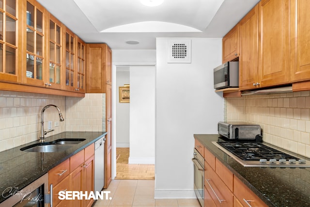 kitchen with a sink, stainless steel appliances, baseboards, tasteful backsplash, and dark stone countertops