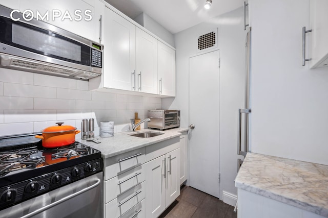 kitchen featuring appliances with stainless steel finishes, tasteful backsplash, white cabinets, a sink, and light stone counters