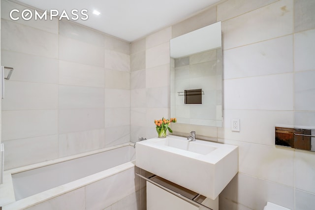 full bath with tile walls, a tub to relax in, and vanity