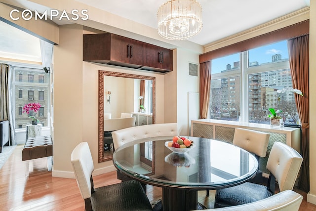 dining room with visible vents, baseboards, light wood-type flooring, a chandelier, and a city view