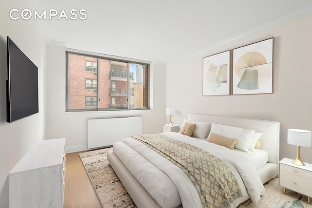 bedroom with radiator heating unit, wood finished floors, ornamental molding, and baseboards