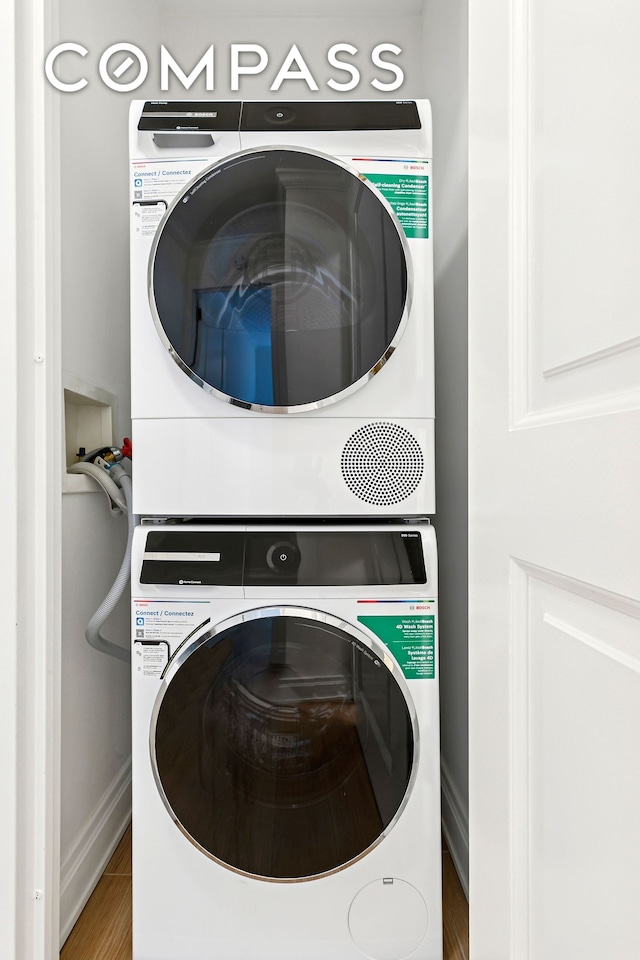 laundry room featuring stacked washer and clothes dryer, baseboards, and wood finished floors