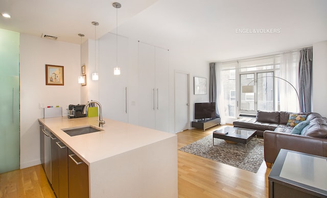 kitchen with pendant lighting, a peninsula, light wood-style floors, open floor plan, and a sink