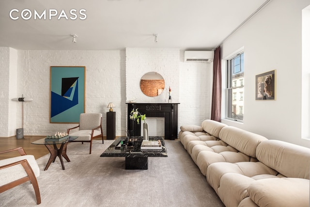 living room featuring wood finished floors, a wall unit AC, brick wall, and a fireplace