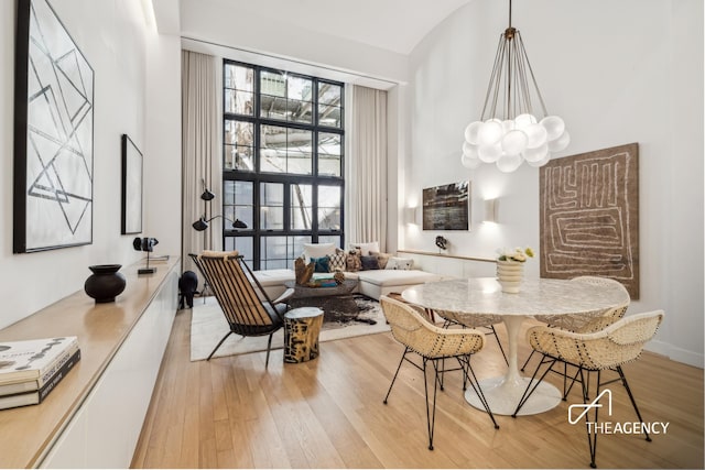 dining area with light wood-type flooring, a chandelier, and vaulted ceiling