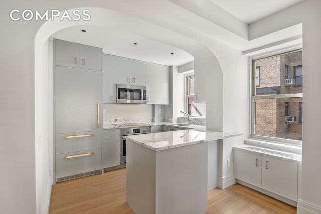 434 E 52nd St Unit 10E, New York City, NY 10022 - kitchen with stainless steel appliances, arched walkways, light stone counters, a peninsula, and light wood-style floors