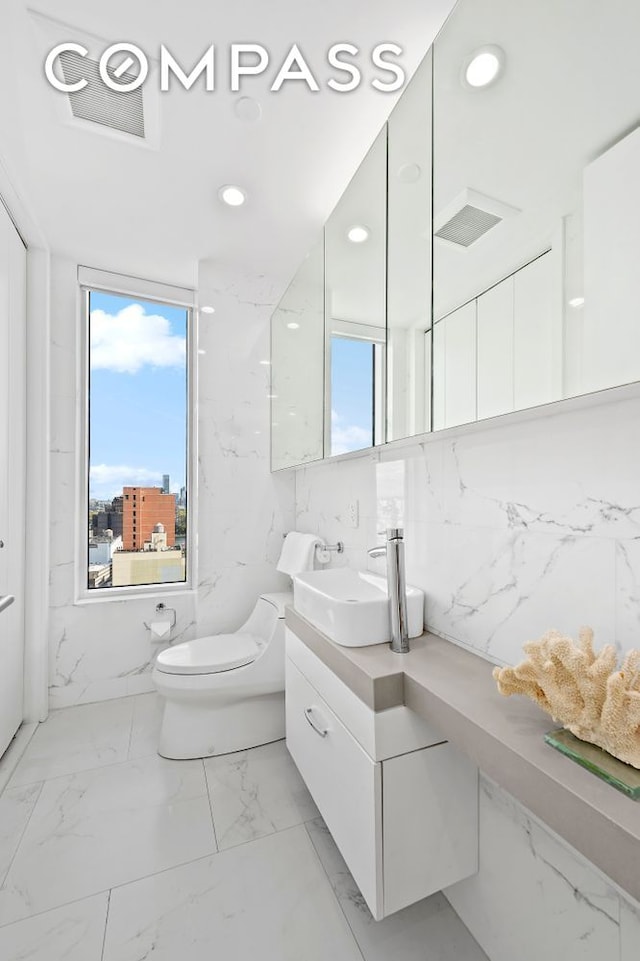 301 E 61st St Unit 16A, New York City, NY 10065 - bathroom with healthy amount of natural light, vanity, marble look tiles, toilet, and recessed lighting