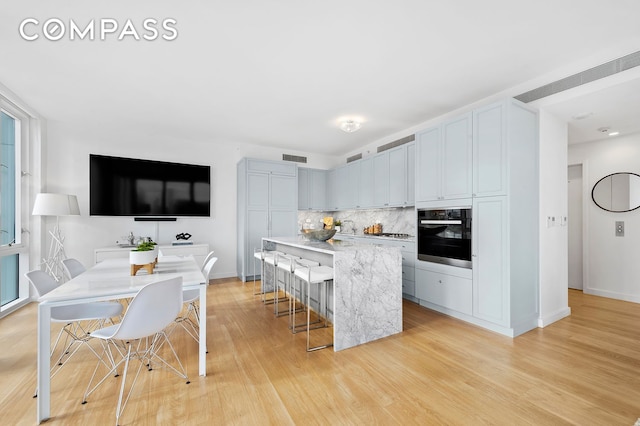 kitchen featuring black oven, backsplash, light wood-style floors, a kitchen bar, and a center island