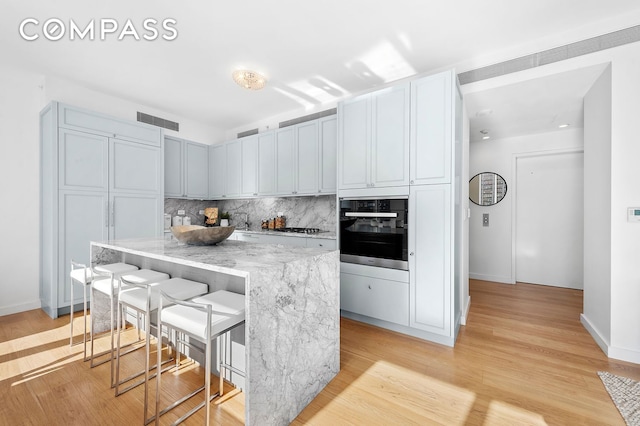 kitchen with oven, backsplash, gas stovetop, light stone countertops, and a breakfast bar