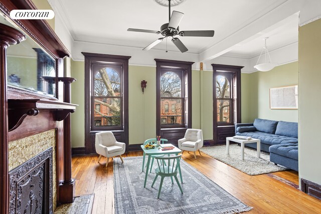 living room with a tiled fireplace, hardwood / wood-style flooring, ceiling fan, and crown molding