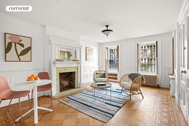 sitting room featuring a fireplace with raised hearth, visible vents, wainscoting, and radiator